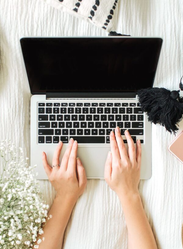 Typing on a laptop with flowers nearby representing freelance writing and content creation.